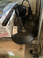 Two black metal wall mount light fixtures placed on a metal shelving unit near cardboard boxes.