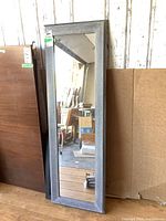 Full view of the rectangular wood framed mirror showing the gray distressed frame and clear mirror surface, standing against a wall in a garage setting.