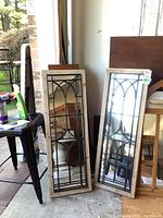 Two rectangular mirrors leaned against a wall in a garage, showing full view with wooden frames and metal decorative grids on glass.