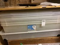 Photo showing two large plastic underbed storage boxes stacked. Bottom box has wheels visible. Both have ribbed lids and are designed for underbed storage.