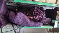 Purple towels, floor mat, faux flowers, purse on wire shelf