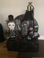 Overview of all items on and around the suitcase including the desk lamp, Edison bulb, incandescent bulbs, sunglasses, desk bell, mirror, and metal art figure