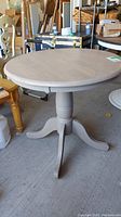 Full round wooden table with pedestal base shown in a garage setting with other furniture around.