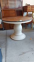 Round wood pedestal table with detached top, showing full table with brown wooden top and white base.