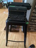 Royal vintage typewriter sitting on a black metal stool on hardwood floor, close-up view of typewriter front and keys