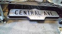 Full view of the long rectangular vintage Central Ave street sign laid flat on the floor, showing the complete text and shape.