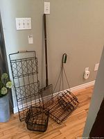 Photo showing multiple wire racks and baskets leaning against wall with a handled rug beater and whisk broom