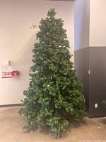 Full view of the tall assembled artificial Christmas tree against a wall, showing full height and overall appearance.