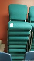 Front view of stacked green fabric upholstered chairs showing cushioned seats and metal frames.
