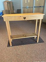 Front view of wooden console table showing heart-shaped cutout on apron and lower shelf.