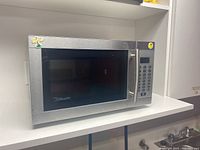 Front left angle view of the stainless steel microwave placed on a white shelf.