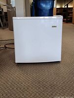 Front view of white Kenmore mini fridge on carpet, showing full front and slightly angled top side.