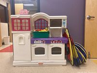 Front view of the Little Tikes kitchen playset with a green bin of plastic foods on the stove and a folded Playhut tent leaning on the side.