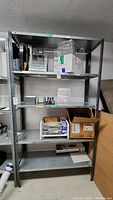 Front view of metal shelf unit with five shelves, loaded with various boxes and office supplies (contents not for sale).