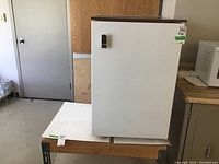 Front view of the white Woods mini fridge on a wooden table.