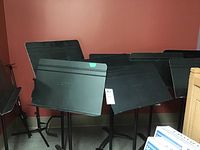 Group of multiple black metal music stands leaning against a wall