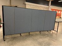 Front view of 7-panel gray fabric room partition on black metal stand with wheels