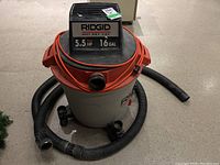 Overall angled view showing vacuum base, wheels, orange lid, black motor housing, hose coiled around base.