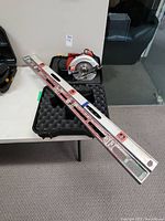 Photo showing Skilsaw circular saw and two aluminum levels resting on a table with carrying case open behind the saw.