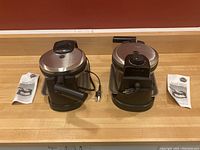 Two waffle irons side by side with instruction manuals on countertop