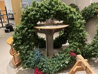 Overall view of large green artificial wreath with red berry decoration and attached string lights, standing leaning on wooden furniture.