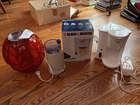 Two Black & Decker coffee makers, Braun grinder and ice cream ball maker on hardwood floor. Box for one Black & Decker coffee maker included.