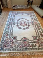 Full view of hand tufted wool area rug from India with floral pattern, cream background, and fringed edges