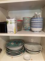 Shelf with blue patterned ceramic bowls stacked with matching soup spoons on top, and white plates and bowls on lower shelf.