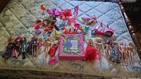 Wide view of all dolls and accessories on mattress including a boxed Barbie playset and pink toy scooter.