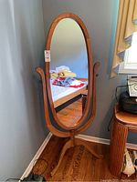Full view of the oval chevalier mirror showing its wooden frame and curved legs base next to a window.