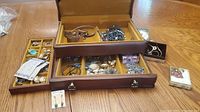 Full view of brown leather-like multi-compartment jewelry box with assorted costume jewelry inside including bracelets, necklaces, brooches, rings, and earrings in multiple trays