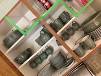Multiple shelves showing stacked dinner plates, mugs, cups, bowls and sugar/creamer under cabinet.