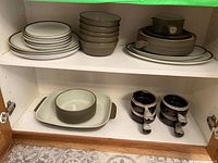 Photo of various Denby dinnerware including stacked plates, multiple bowls, and covered casserole with sauce dish and French onion bowls on bottom shelf.