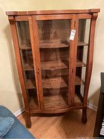 Front view of the wood display cabinet showing glass-paneled doors, curved legs, and four shelves.