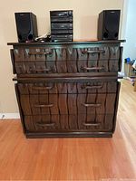 Front view of the dark wood dresser showing five drawers with carved fronts and curved wooden handles. Electronics (speakers, stereo) placed on top of dresser not included.
