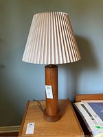 Front view of the lamp showing full height, wood base, and pleated shade on a wood table.