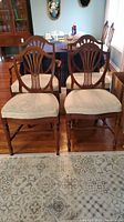 Four armless dining chairs grouped front view on floor showing shield backs and upholstered seats.