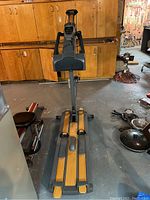 Full view of NordicTrack cross country skiing exercise machine in basement, showing overall device with foot platforms, handle poles, and digital console.
