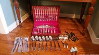 View of full lilac time pattern silver plated set arranged on hardwood floor, inside red lined canteen box with extra cutlery pieces laid out.