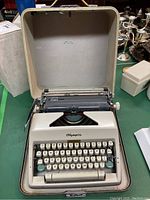 Full view of Olympia typewriter inside hard carrying case, showing keyboard, ribbon mechanism and case interior.