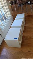 Three white cube storage units lined up on hardwood floor.