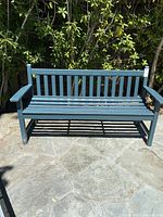 Front view of full green wooden bench on stone patio