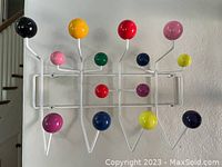 White metal wire frame coat rack with fifteen multicolored spherical hooks mounted on wall