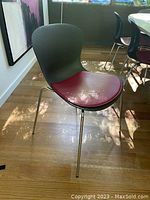 Three-quarter front view of one chair showing grey shell, red leather cushion and steel legs