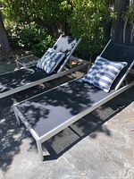 Two lounge chairs with striped pillows on stone patio.