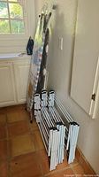 Two ironing boards leaning vertically against a wall, three folded collapsible clothes drying racks stacked on the floor next to the boards.