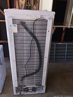 Rear of Danby refrigerator showing condenser coils, attached power cord, and product labels including model info.