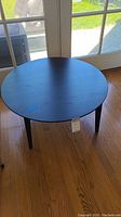 Front view of round black wooden table with four tapered legs on hardwood floor