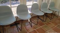 Five gray molded plastic chairs in a row facing camera against windowed wall