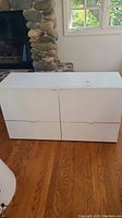 Front view of white storage cabinet with 4 drawers and smooth finish against wooden floor.